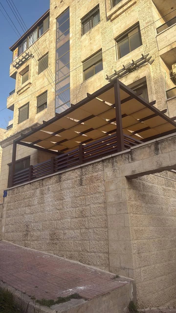 برجولة على تراس مرتفع بإطار خشبي اللون وشرائح معدنية